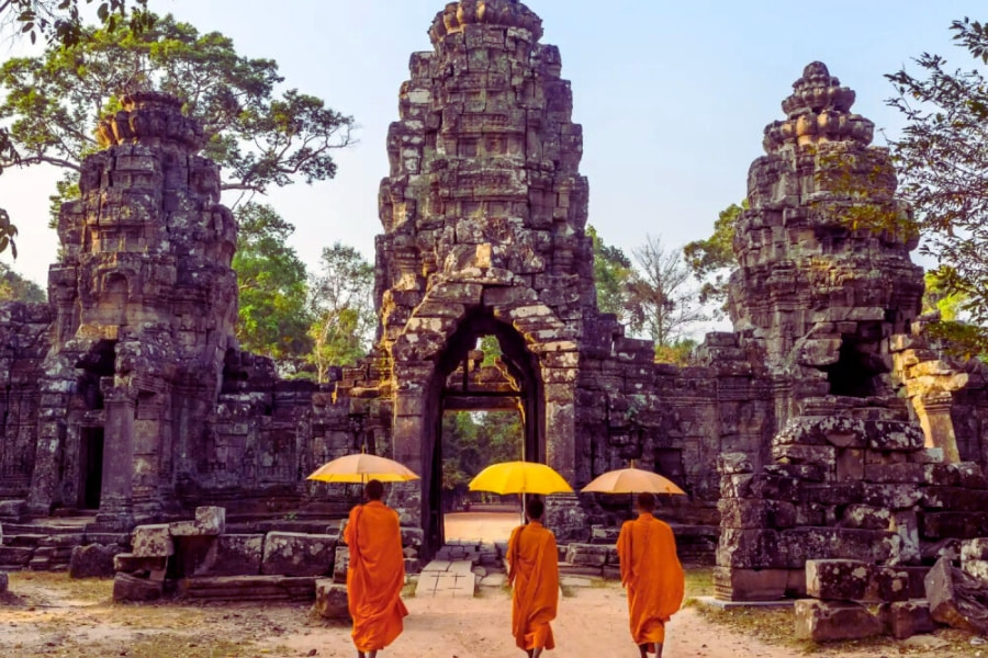 Buddhist monks with yellow umbrellas walking through Angkor temple ruins – Auasia Travel